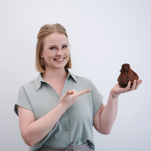 Juliane Krumbiegel lächelt und hält das symbolische Mama Mojo Säckchen in der Hand – Symbol für Klarheit, Selbstfürsorge und Leichtigkeit im Mama-Alltag.