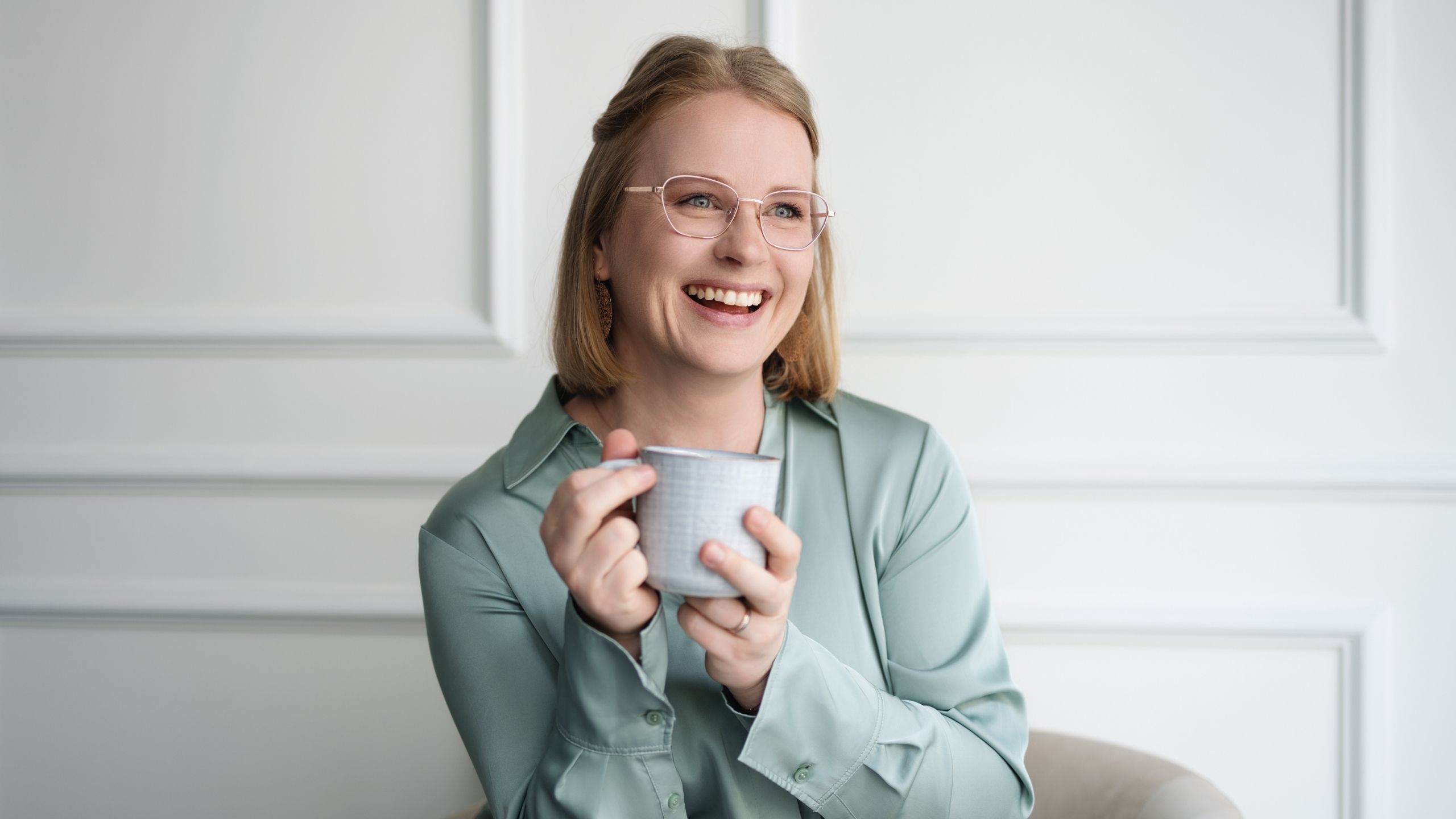 Juliane Krumbiegel, Gründerin von Mama Mojo, sitzt lachend mit einer Tasse in der Hand. Authentisches Portrait, das Nähe, Wärme und Lebensfreude ausstrahlt.